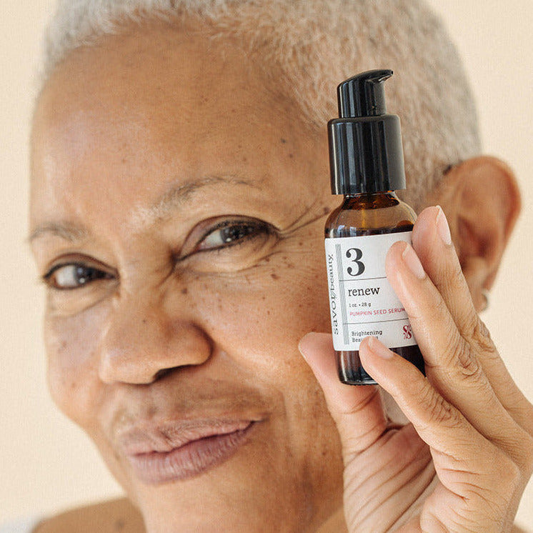 Woman holding a skincare product bottle against her face on a beige background