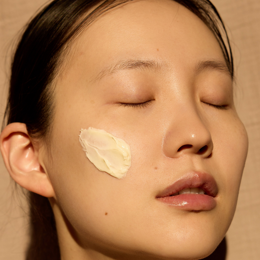 Woman with a skincare product on her cheek against a beige background