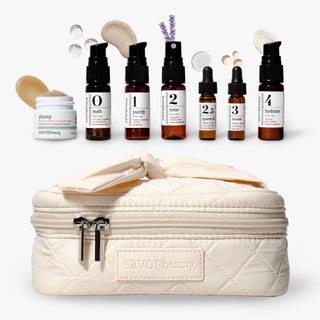 Savor Beauty's glass skin discovery kit skincare arranged on a white background, featuring five amber dropper bottles labeled 0 to 4, with texture shots, and a quilted cream zip case with a bow. 