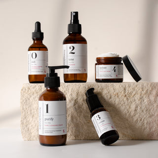 5 skincare products with labeled bottles on a stone surface and cream backround