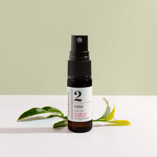 Small spray bottle labeled '2' with a green leaf on a white surface and light green background