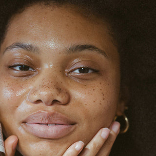 Woman holding a skincare bottle near her face against a neutral background