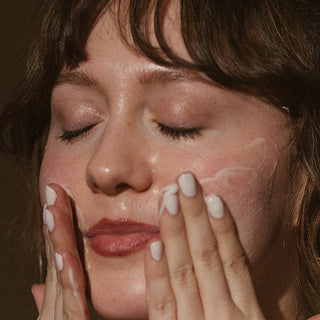 Woman applying face wash to her face against a dark background