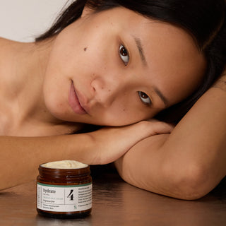 Woman lying down with a jar of fragrance-free Truffle Face Cream on a table