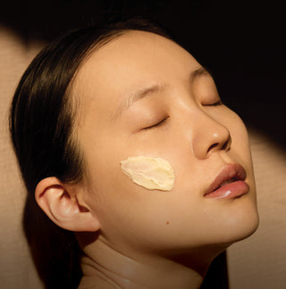 Woman with a skincare product applied to her cheek against a neutral background