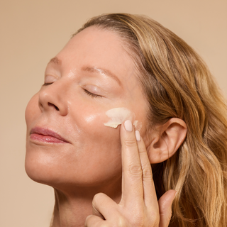 Woman applying cream to her face with a neutral background