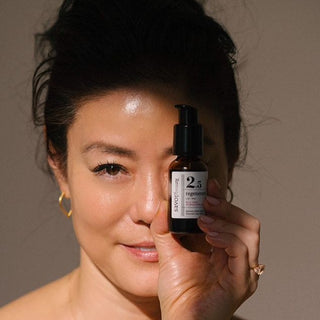 Founder Angela Jia Kim holding a blue tansy regenerate serum bottle near her face against a neutral background