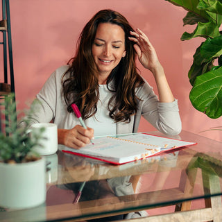 Middle aged woman writing on a glass desk in her Savor Beauty Planner 