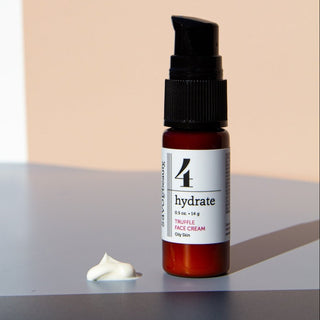 travel size truffle face cream bottle on grey and peach background.